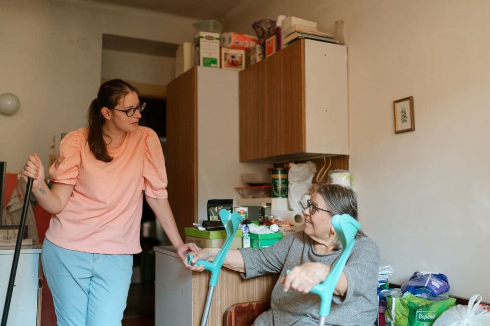 A carer supporting an older man using crutches in his kitchen
