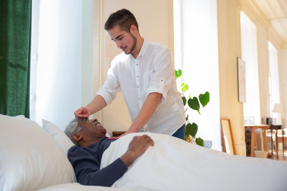A carer helping an older man settle comfortably in bed