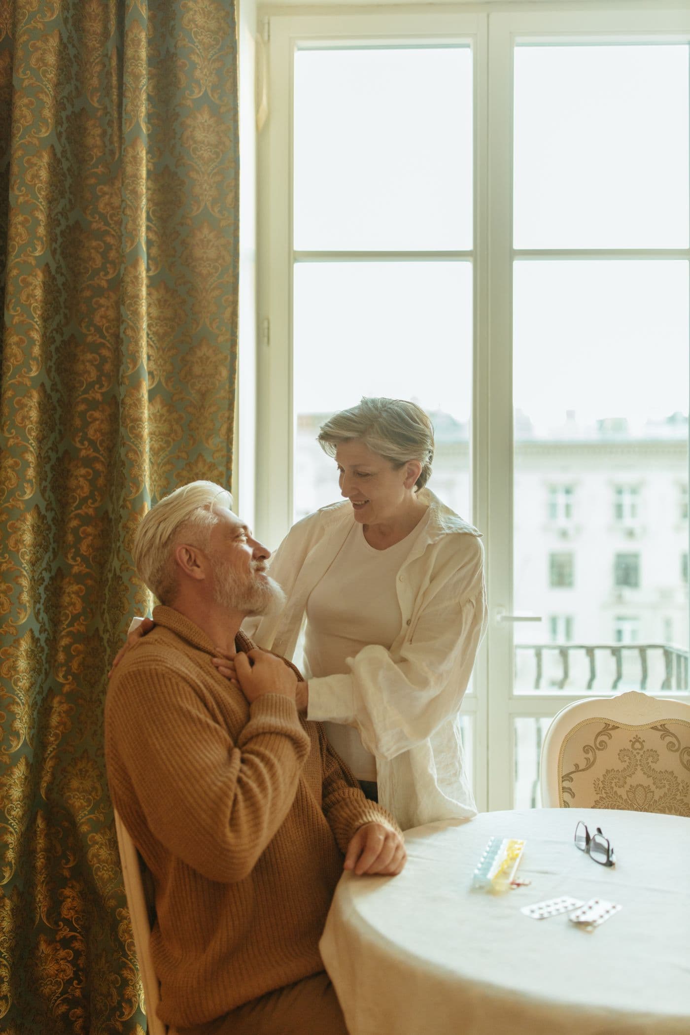An older couple sitting together at a table beside a window